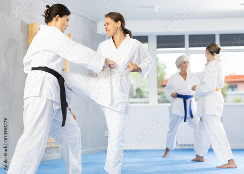 Women in white kimonos are engaged in wrestling at sports training. Woman paired up with female partner performs classic techniques of repelling blow in karate technique