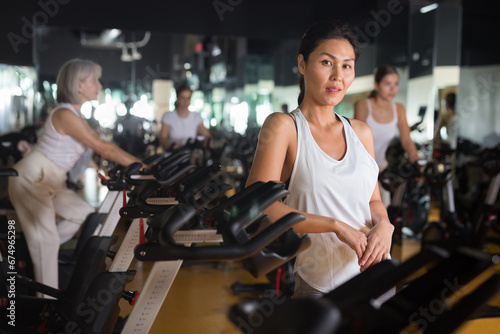 Portrait of confident asian woman posing near fitness bike in gym indoor