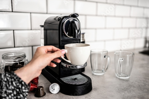 Girl hand with capsule coffee machine and white cup at kitchen. Woman preparing italian caffeine beverage using professional espresso maker