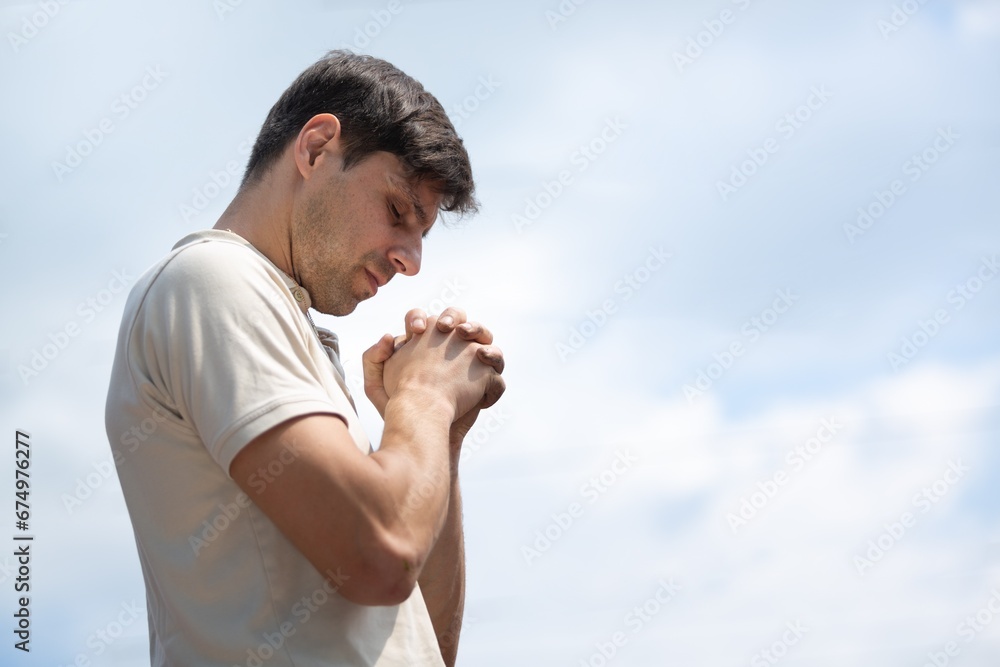 Young man praying to God on sky background.