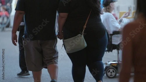 This video shows a close up, rear view of a fat obese couple walking by in slow motion.