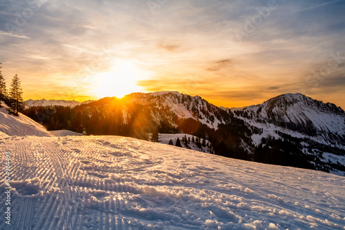 Winter landscape on Klewenalp mountain in Swiss Alps, Switzerland at sunset. Popular ski slope and winter sport attraction with snowy mountains, fir trees and setting sun