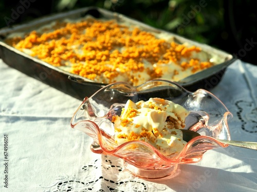 Closeup of ice cream in a glass with a tray of cake on a tablecloth outdoors