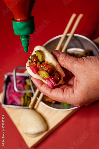 Man holding bao oriental sandwich vlose up red background top view