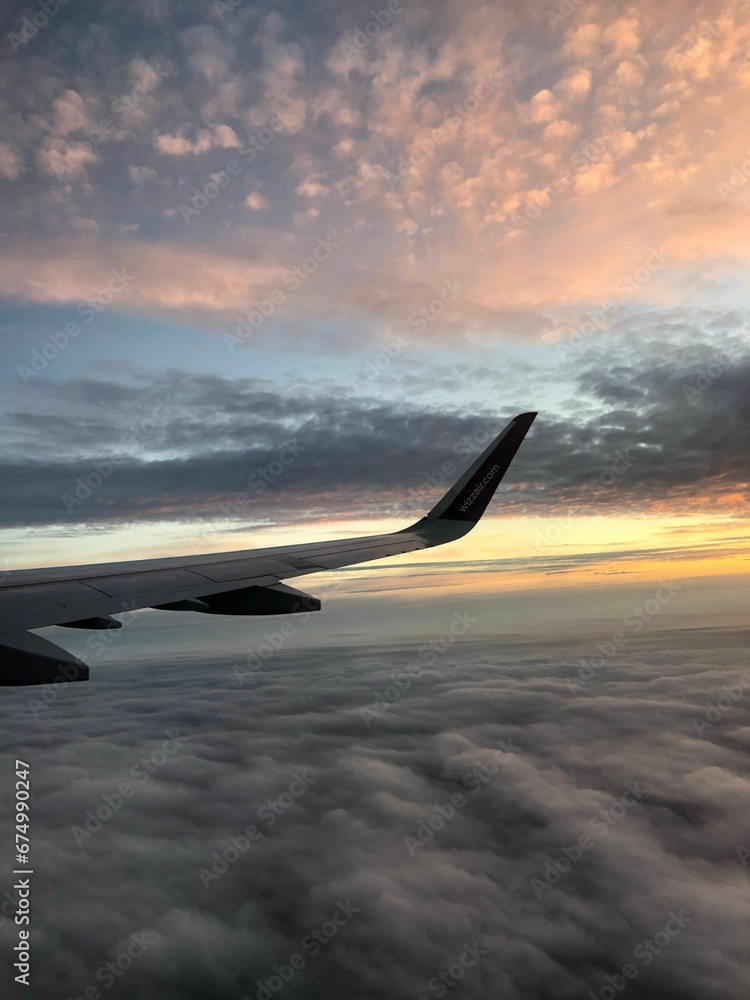 Wing of the airplane slicing through the clouds at sunset Wing of the airplane slicing through the clouds at sunset