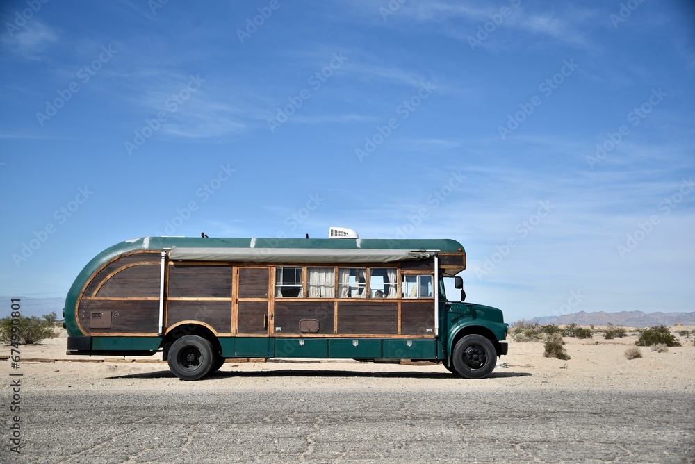 Aged green school bus on a dirt road in the desert against a blue sky