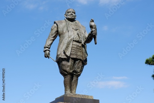 Bronze statue of a man with a bird in his hand against a clear sky in the background