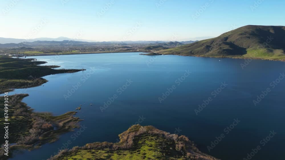 Aerial video of the lake surrounded by the rocky mountains covered with green grass Aerial video of the lake surrounded by the rocky mountains covered with green grass