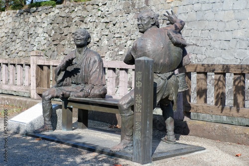Bronze statue of two men seated on a bench in a park