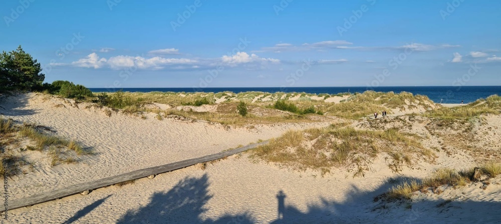Stunning beach scene with a sandy path flanked by green grass on a sunny day