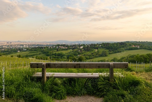 Canvas Print Wooden bench overlooking a grassy field with a picturesque view of Vienna in the