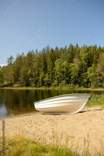 Boat on the lakeside under blue sky. © Wirestock