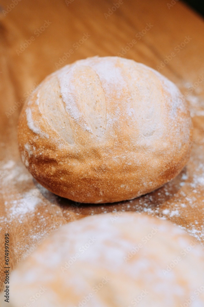 Freshly-baked bread resting on a wooden table top, with a light dusting of flour Freshly-baked bread resting on a wooden table top, with a light dusting of flour