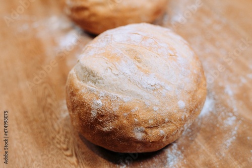 Single freshly-baked bread roll on a wooden background, lightly dusted with flour