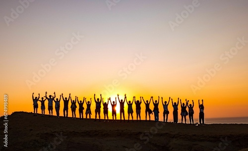 Group of cheerful people having fun on the cliff silhouetted against the sunset