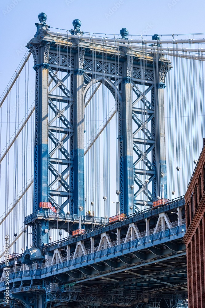 Obraz premium Vertical shot of the Manhattan Bridge between buildings in the Dumbo neighborhood in Brooklyn, NYC