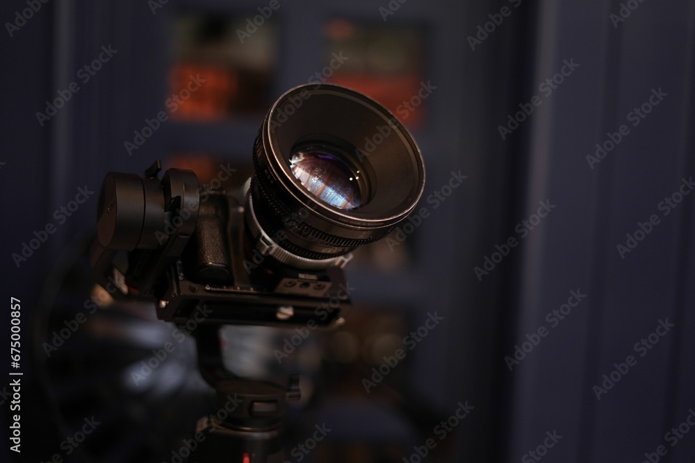 Standard video camera is mounted to a black tripod and is set up in a dark environment.