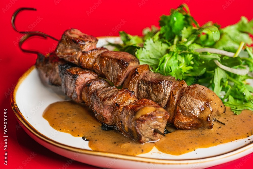 Closeup of grilled meat with sauce and greens on a red background Closeup of grilled meat with sauce and greens on a red background