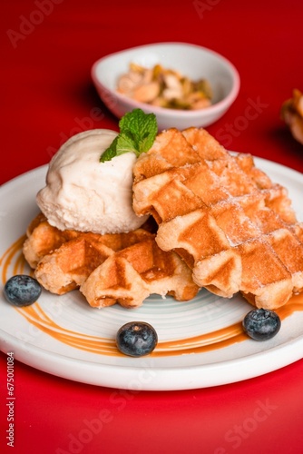 Closeup of waffles served with ice cream and blueberries on a red background