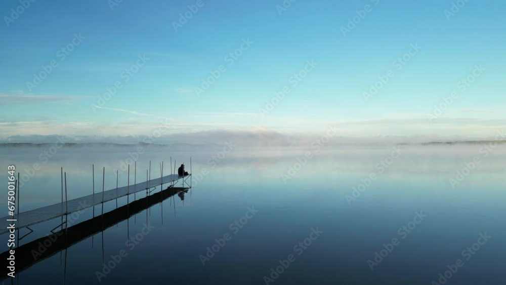 Aerial video of a person on a pier looking at the calm water on a foggy day Aerial video of a person on a pier looking at the calm water on a foggy day