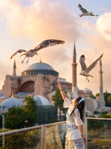 Lifestyle, Asian woman tourist feeding seagulls at view point in vacation. There is a Hagia Sophia or Ayasofya Mosque in background in a blur. Popular tourist destination. Istanbul, Turkiye, Turkey photo