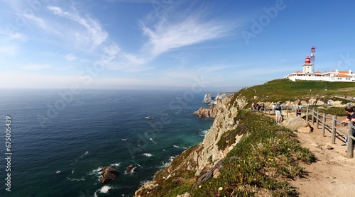 People on a cliff, looking out at the horizon and a distant lighthouse. Cabo da Roca, Portugal.