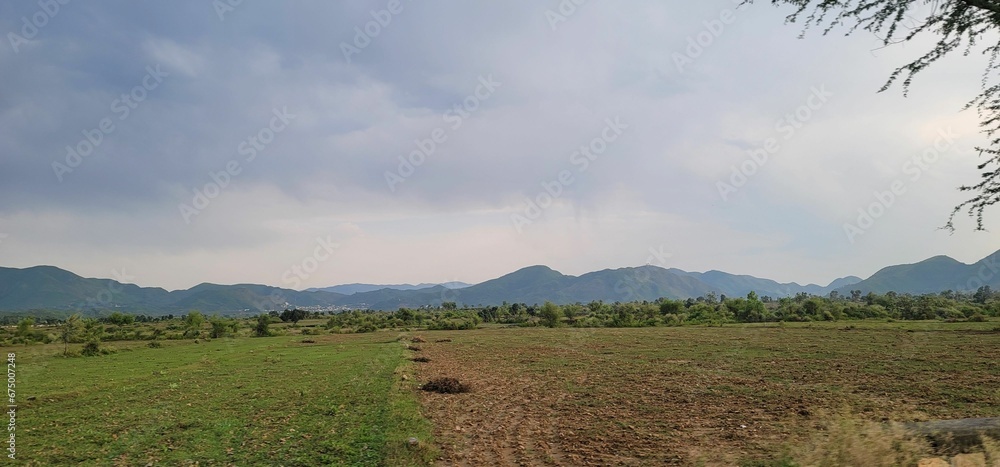 a rural area with mountains in the distance and a cloudy sky