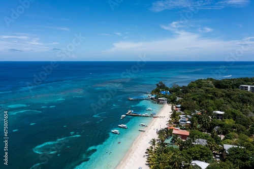 Aerial view of a coastal beach with crystal blue waters and white sand shoreline in Roatan Honduras