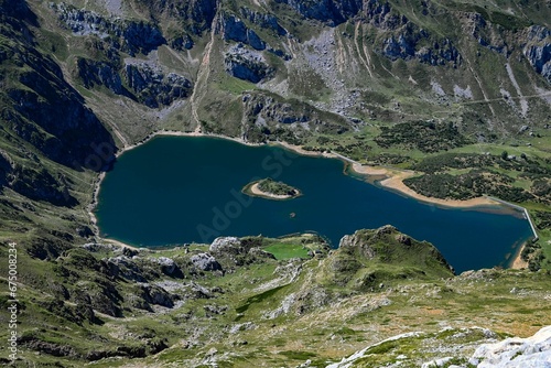 Fototapeta Naklejka Na Ścianę i Meble -  Large lake nestled at the foot of a majestic mountain range, surrounded by lush greenery