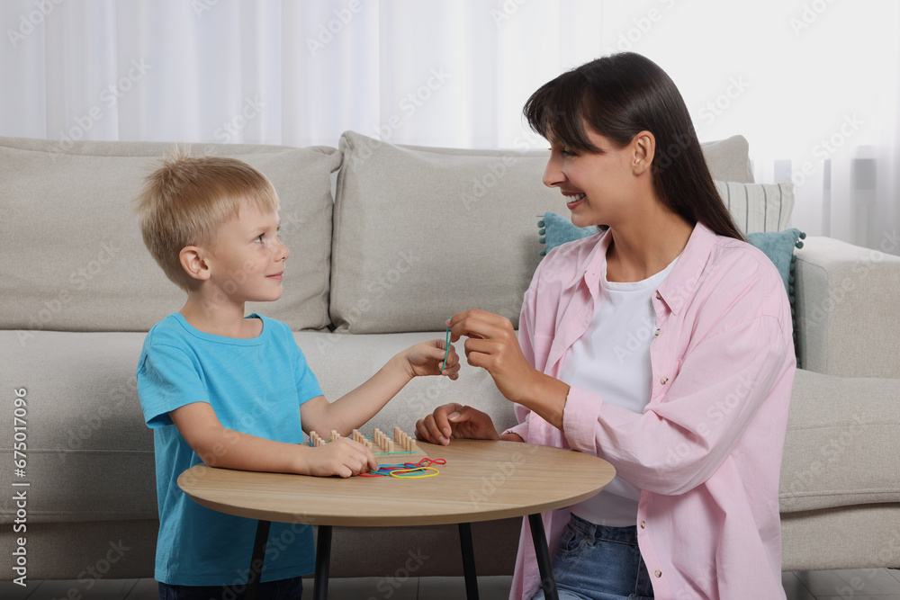 Motor skills development. Happy mother helping her son to play with geoboard and rubber bands at coffee table in room Motor skills development. Happy mother helping her son to play with geoboard and rubber bands at coffee table in room