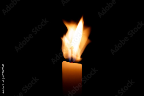 Photograph of lit candle with agitated fire on black background.
