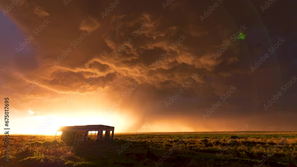 A thunderstorm overtakes an abandoned gas station as a sunset illuminates the under side of the storm.