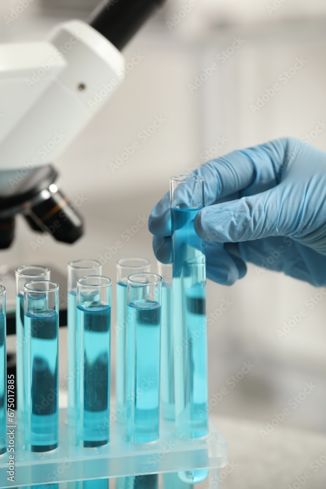 Scientist taking test tube with light blue liquid in laboratory, closeup Scientist taking test tube with light blue liquid in laboratory, closeup