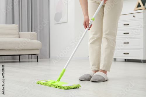 Woman cleaning dirty white parquet floor with mop at home, closeup. Space for text
