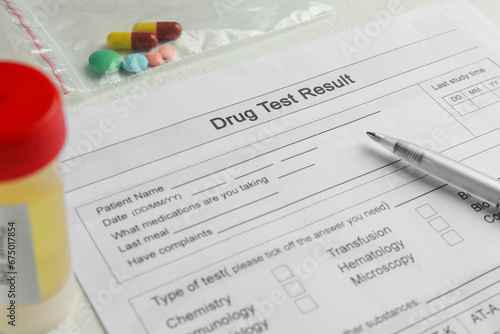 Drug test result form, pills and container with urine sample on light table, closeup