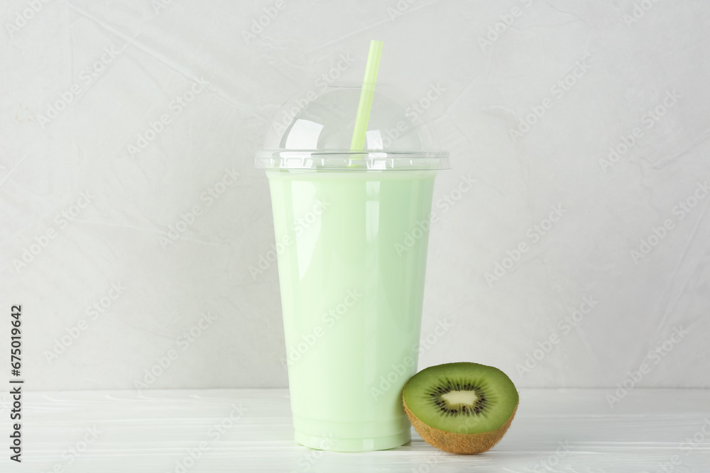Plastic cup of tasty smoothie and fresh kiwi on white wooden table Plastic cup of tasty smoothie and fresh kiwi on white wooden table