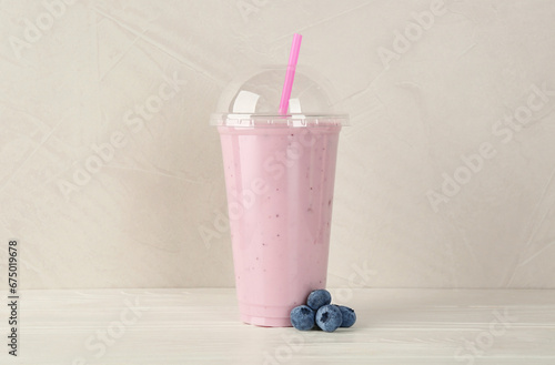 Plastic cup of tasty smoothie and fresh blueberries on white wooden table