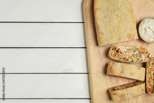 Tasty strudel with chicken, vegetables and sauce on white wooden table, top view. Space for text