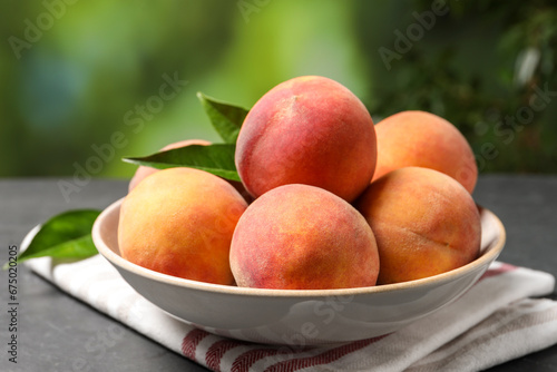 Fresh peaches and leaves in bowl on grey table against blurred green background, closeup