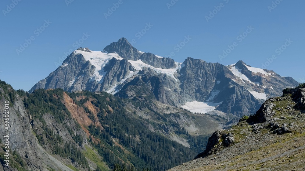 Scenic view of a majestic mountain, with its snow-capped peaks stretching high into the blue sky Scenic view of a majestic mountain, with its snow-capped peaks stretching high into the blue sky