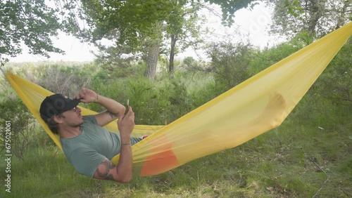 A Man Relaxing in a Hammock is Looking at His Phone - Static Shot photo