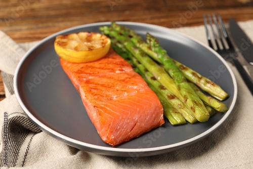 Tasty grilled salmon with asparagus and lemon served on table, closeup