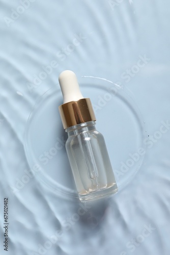 Bottle of cosmetic serum and water on light blue background, top view