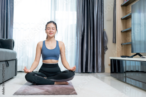 Calm of wellness Asian young woman sit on yoga mat,Yoga meditation of young healthy woman relax and comfortable at white cozy home,Yoga Exercise for Wellness Concept.