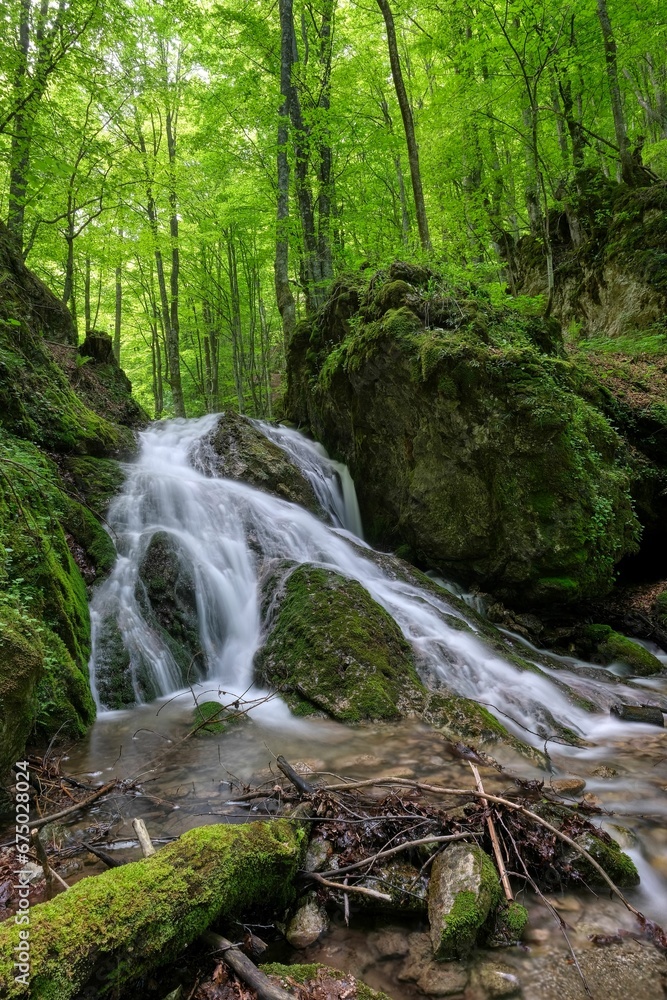 Scenic view of a waterfall cascading down the mossy rocks in a forest Scenic view of a waterfall cascading down the mossy rocks in a forest