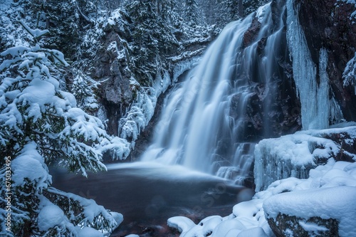 frozen waterfall in a snowy forest with trees and rocks on either side