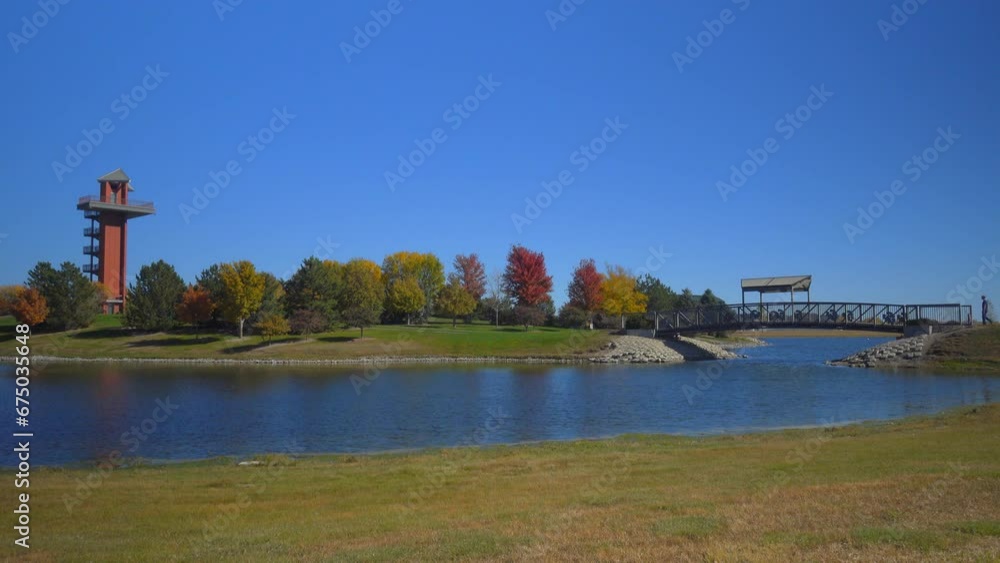 A man walking across a bridge over a pond toward a watchtower. A man walking across a bridge over a pond toward a watchtower.