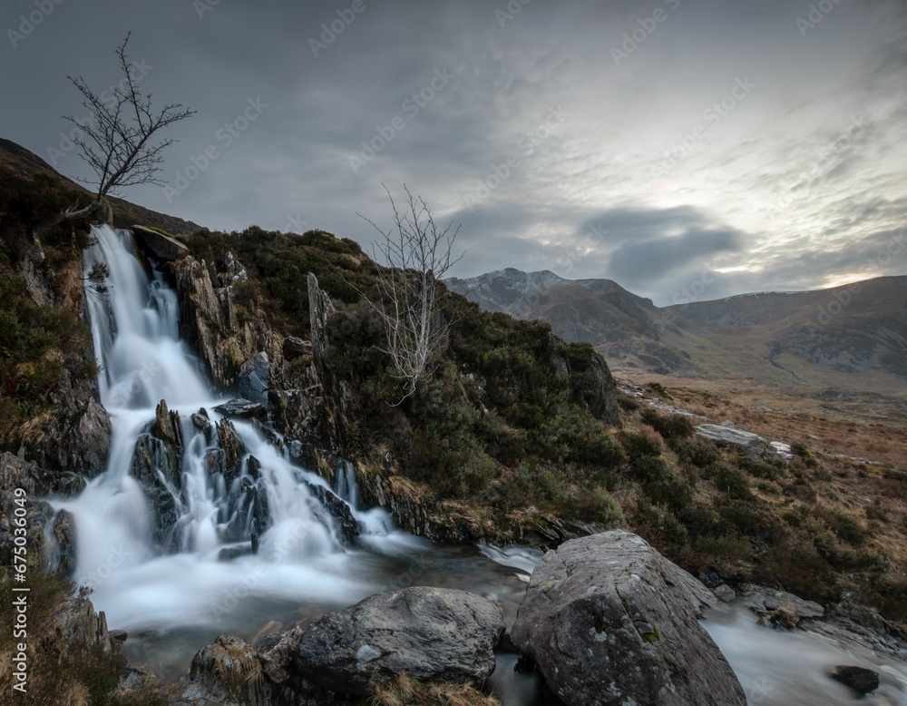 Fototapeta premium Majestic waterfall cascades down a rugged hillside in the Y Garn Mountains of Wales