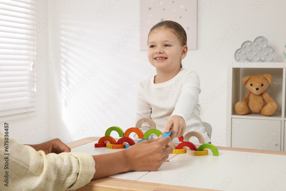 Motor skills development. Mother helping her daughter to play with colorful wooden arcs at white table in room Motor skills development. Mother helping her daughter to play with colorful wooden arcs at white table in room