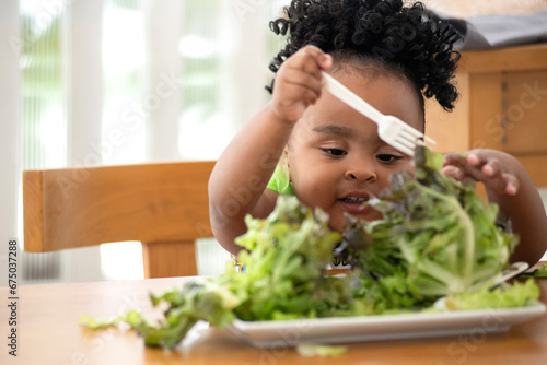 Cute little African girl likes to eat green vegetables, use her hands to pick up lettuce and put it in her mouth photo